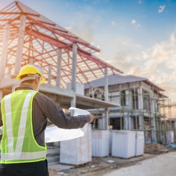 Professional engineer architect worker with protective helmet and blueprints paper at house building construction site background